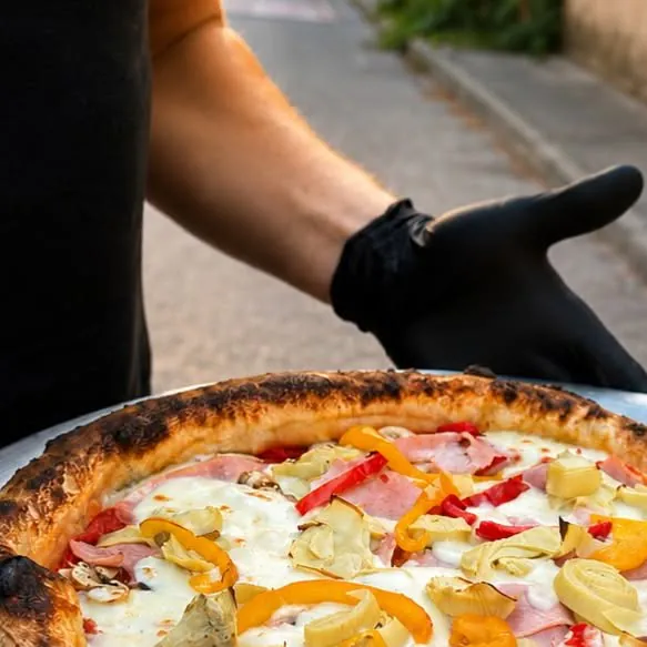 Un pizzaiolo ganté présente une pizza artisanale garnie, préparée le jour même chez Le Retro à Coudoux