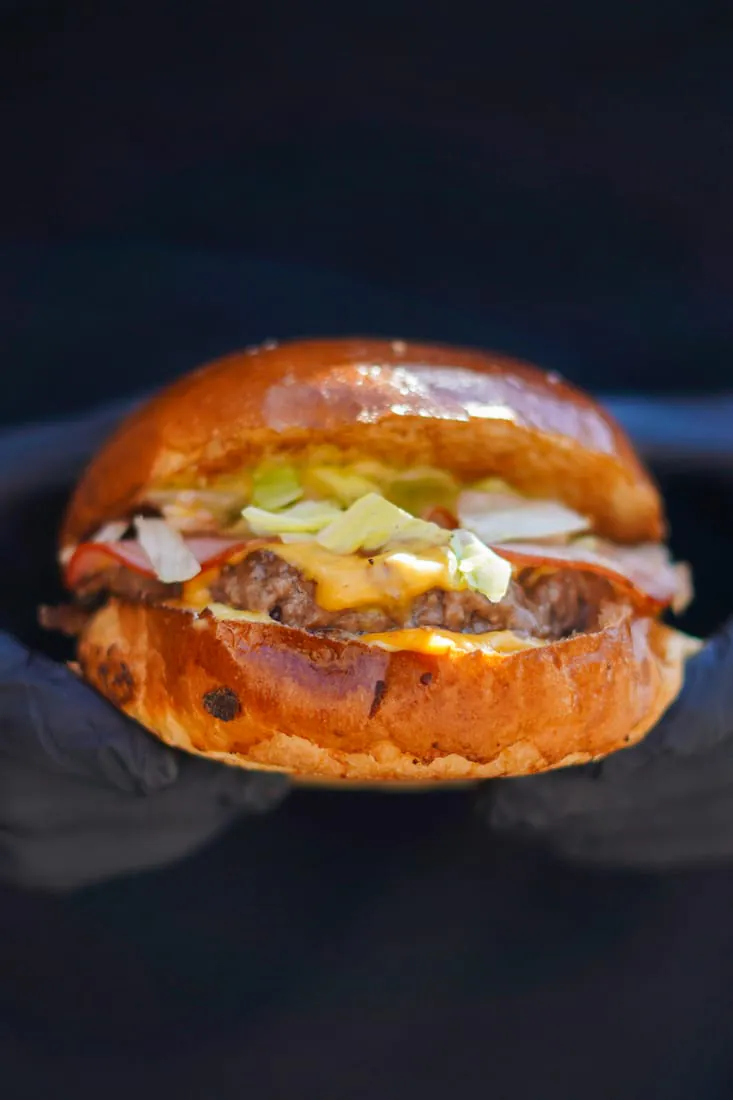 Burger du Retro tenu à la main, steak, cheddar fondu et salade sur pain maison