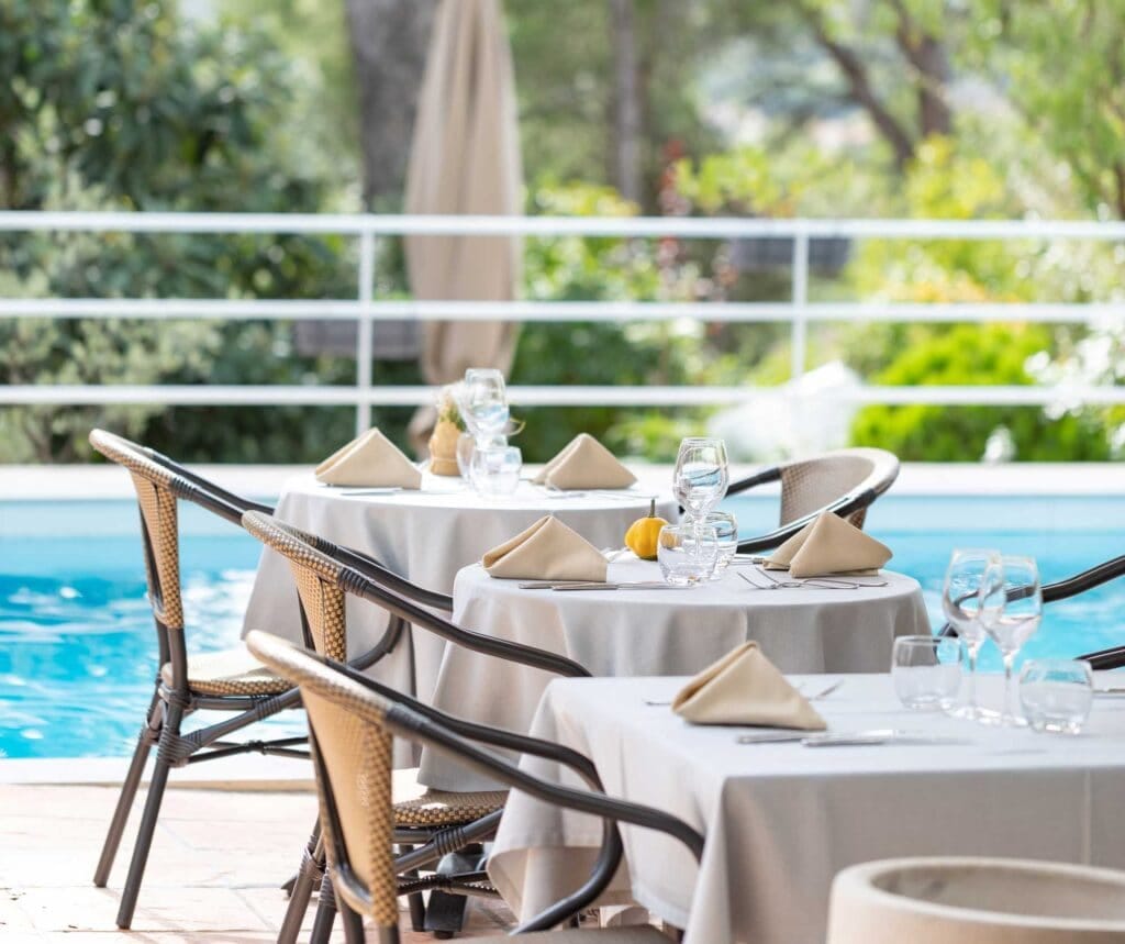 Terrasse gastronomique dressée au bord de la piscine sous les pins