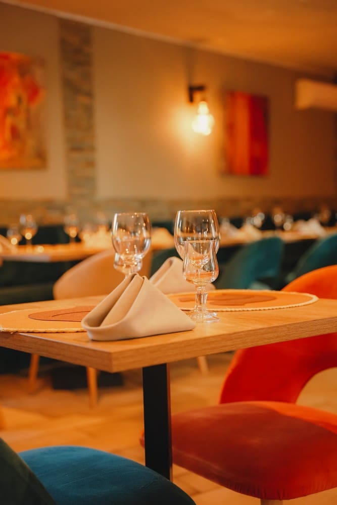 Salle de restaurant provençale dressée, chaises colorées et verres à vin