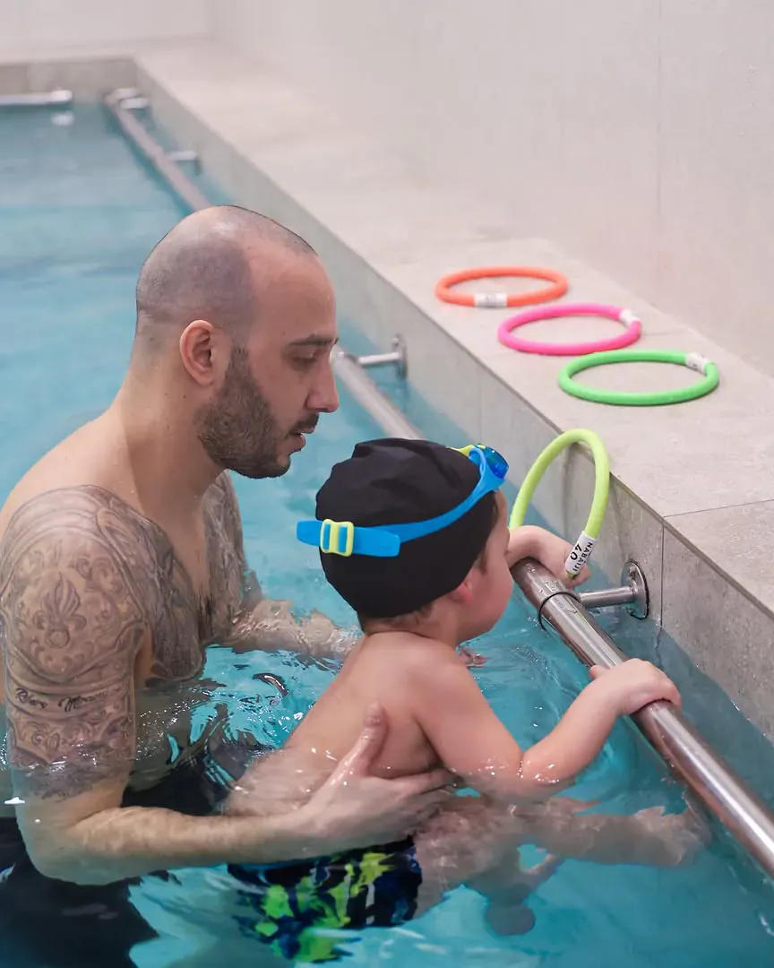 Un maître-nageur Agua Mundo accompagne avec douceur un enfant accroché au bord du bassin à Marseille