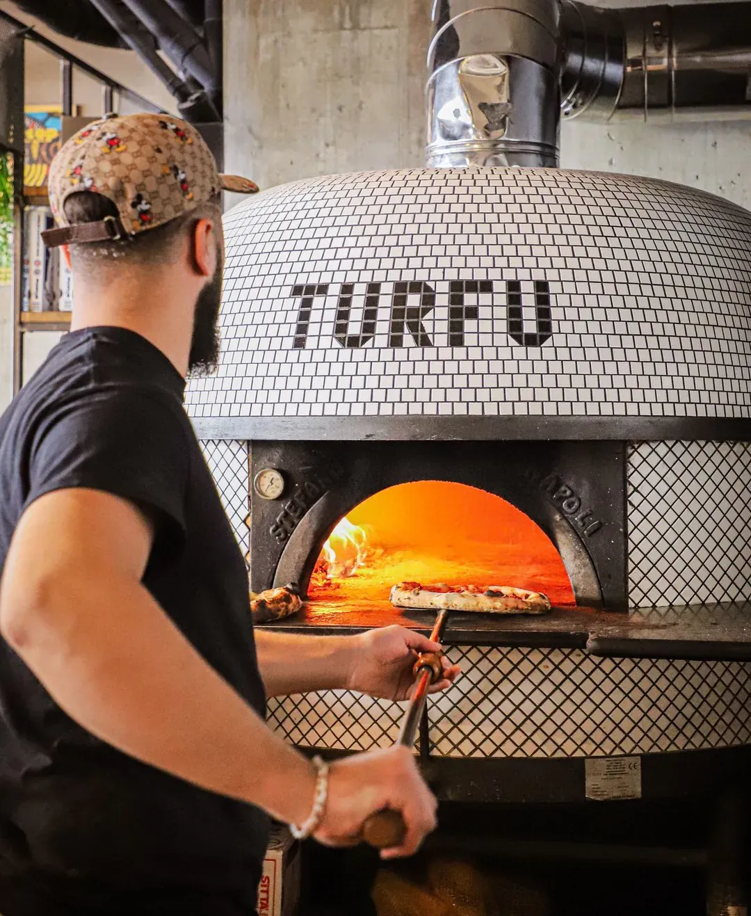 Pizzaiolo enfournant une pizza à la pelle dans un four à bois