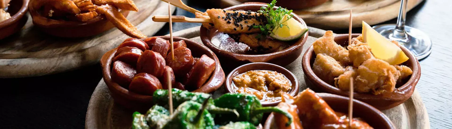 Assortiment de tapas variées servies dans des bols en terre cuite sur des plateaux en bois
