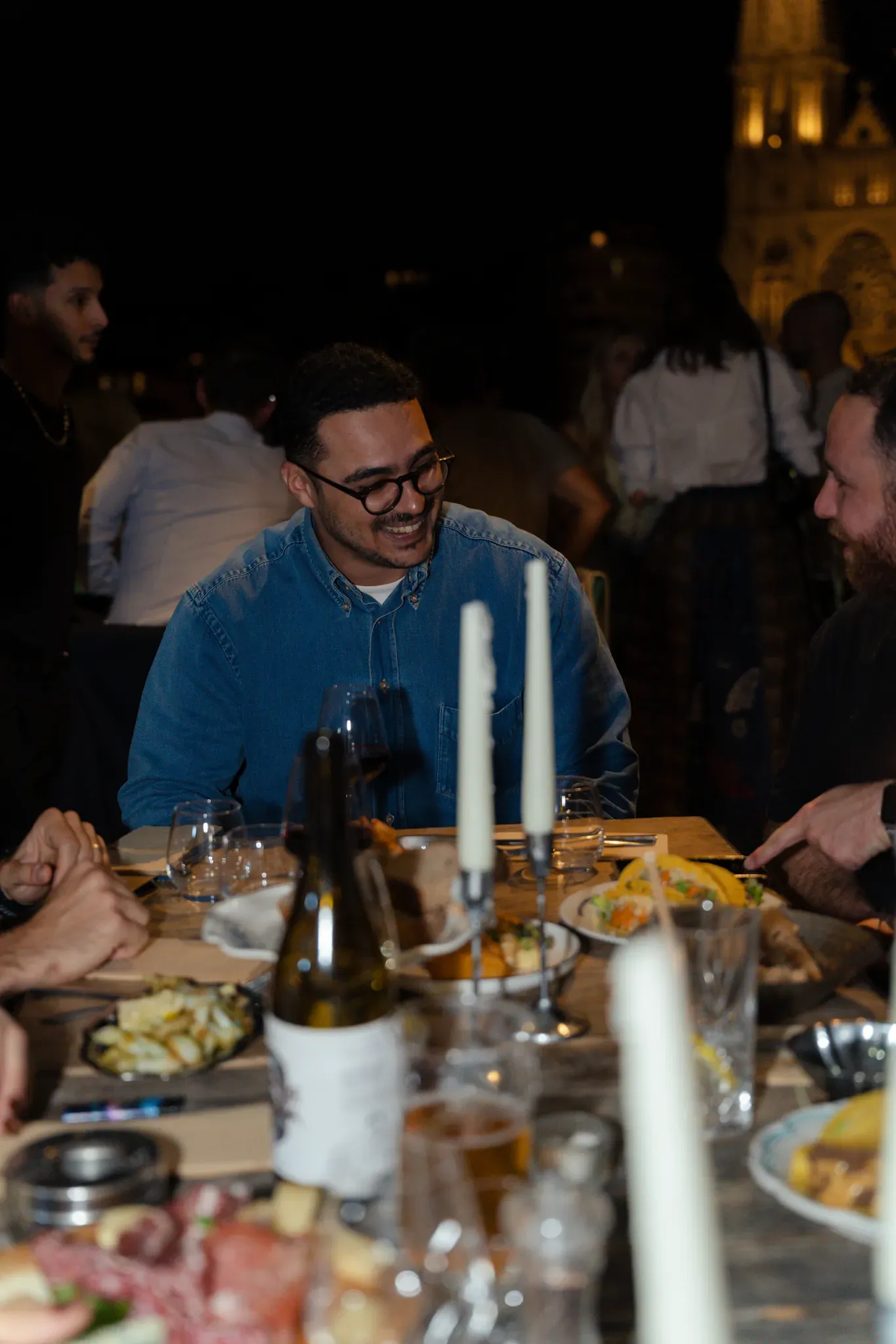 Dîner aux bougies, convives souriants devant l'église illuminée