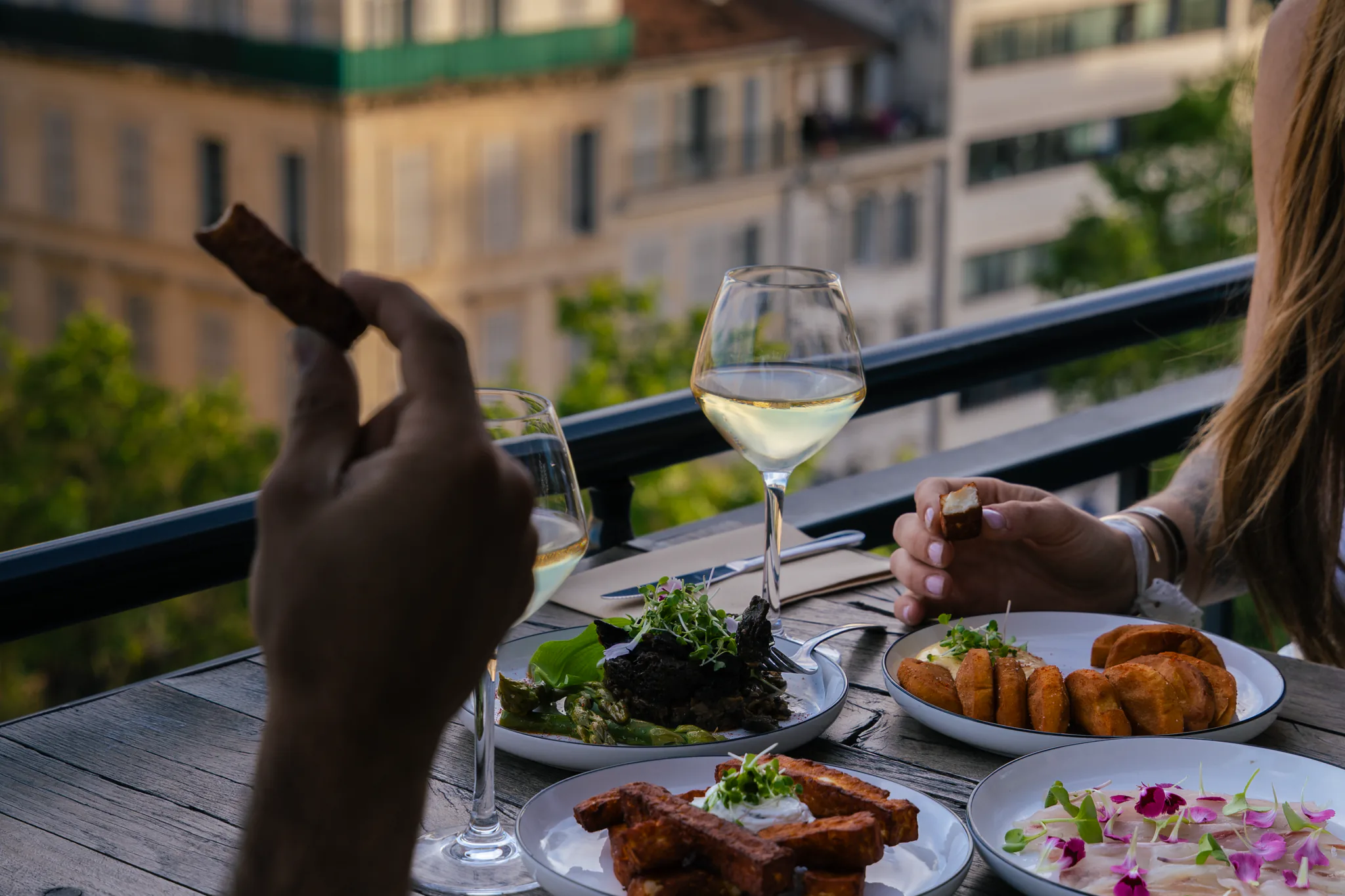 Convives attablés en terrasse devant des assiettes et un verre de vin blanc, vue sur les toits de Marseille au couchant