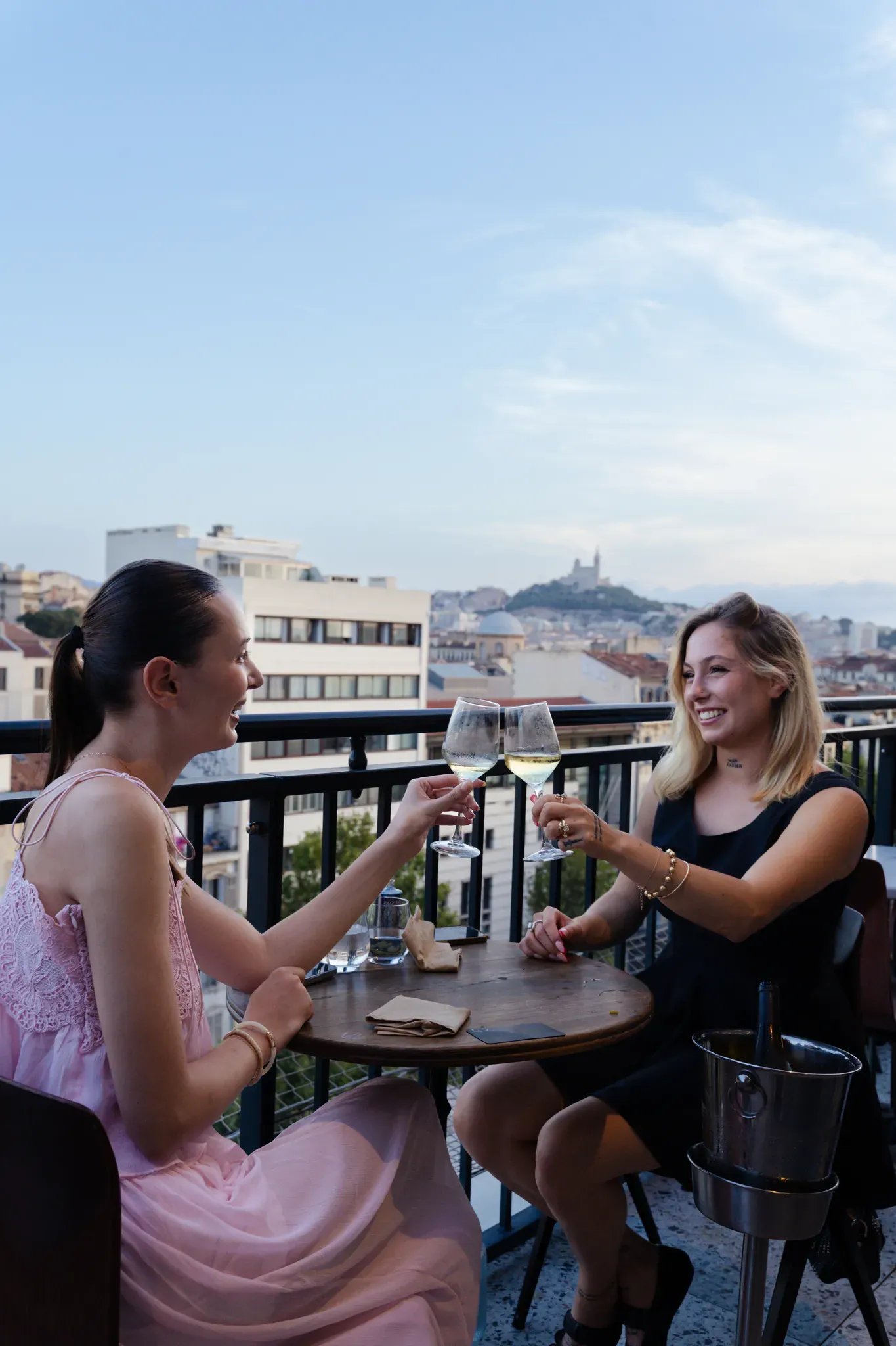 Deux amies trinquent au vin blanc en terrasse, Notre-Dame de la Garde au loin