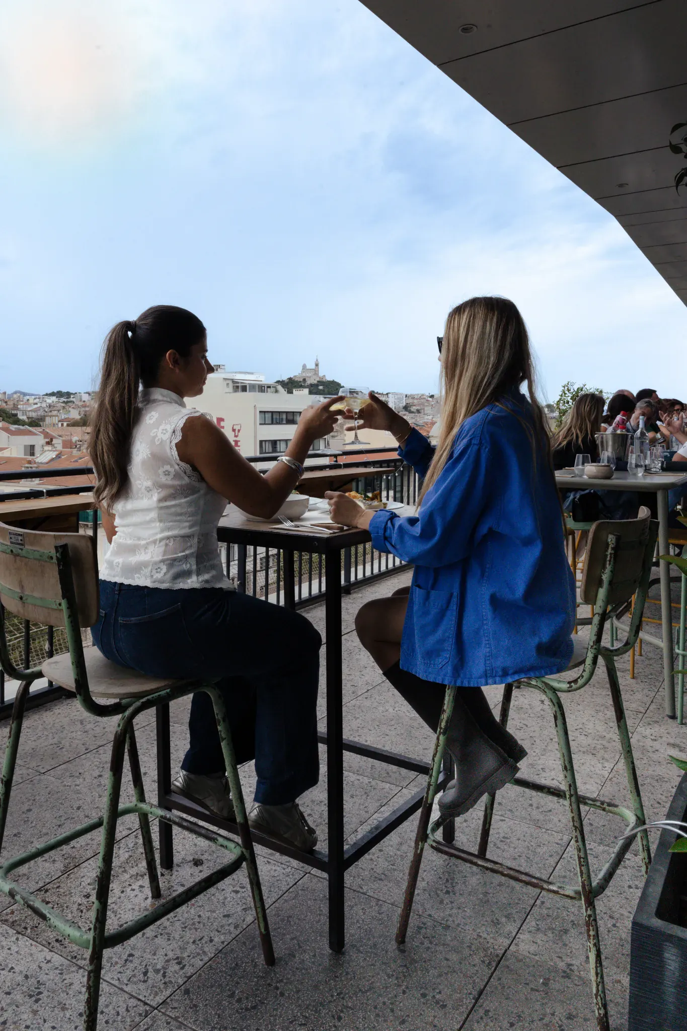 Deux amies aux tables hautes de la terrasse, face à la ville