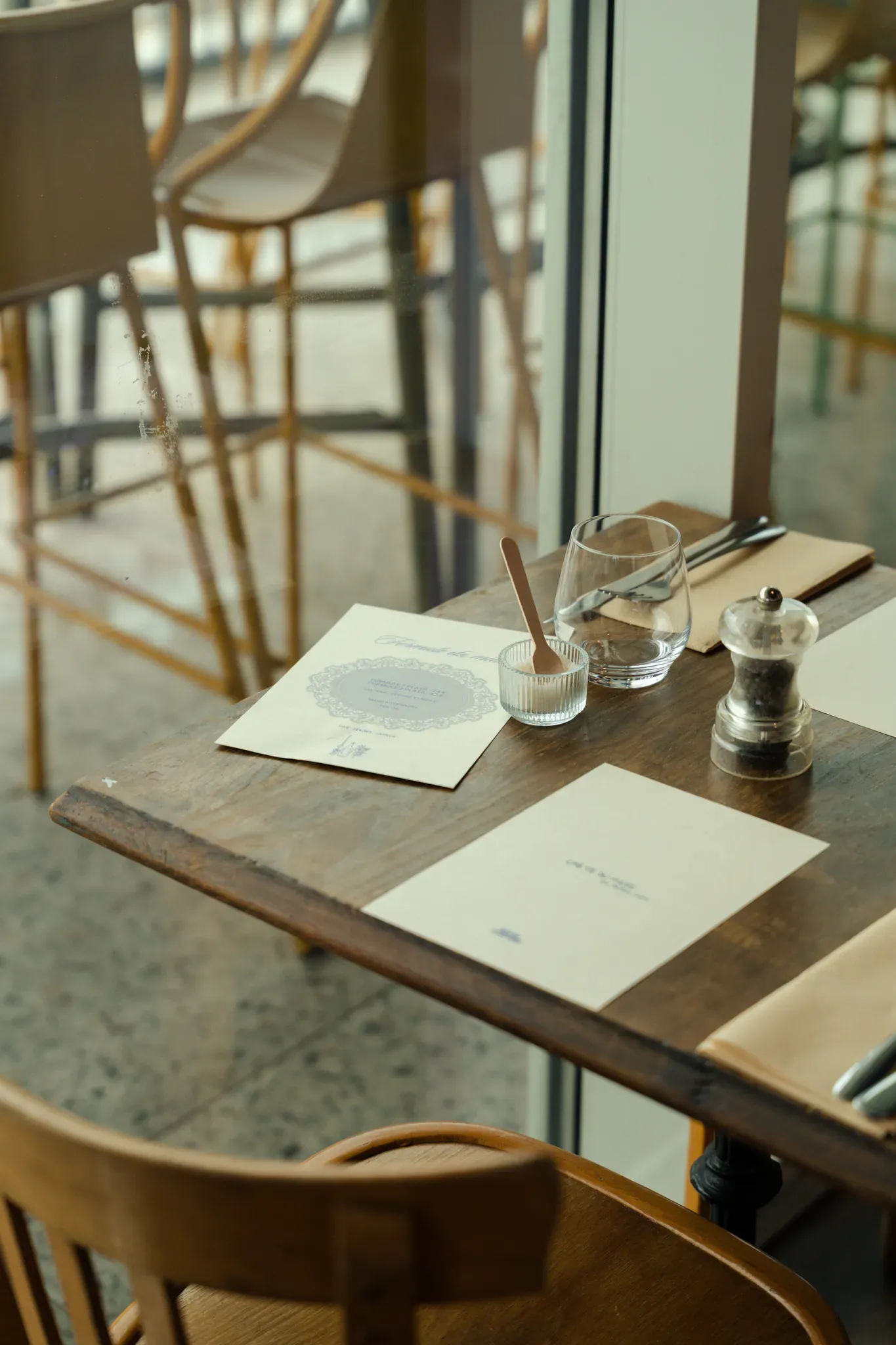 Table dressée près de la baie vitrée : menus, verres et moulin à poivre
