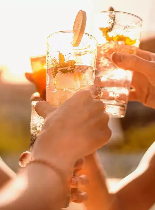 Des mains portent un toast avec des cocktails glacés garnis de tranches d'orange dans une lumière dorée