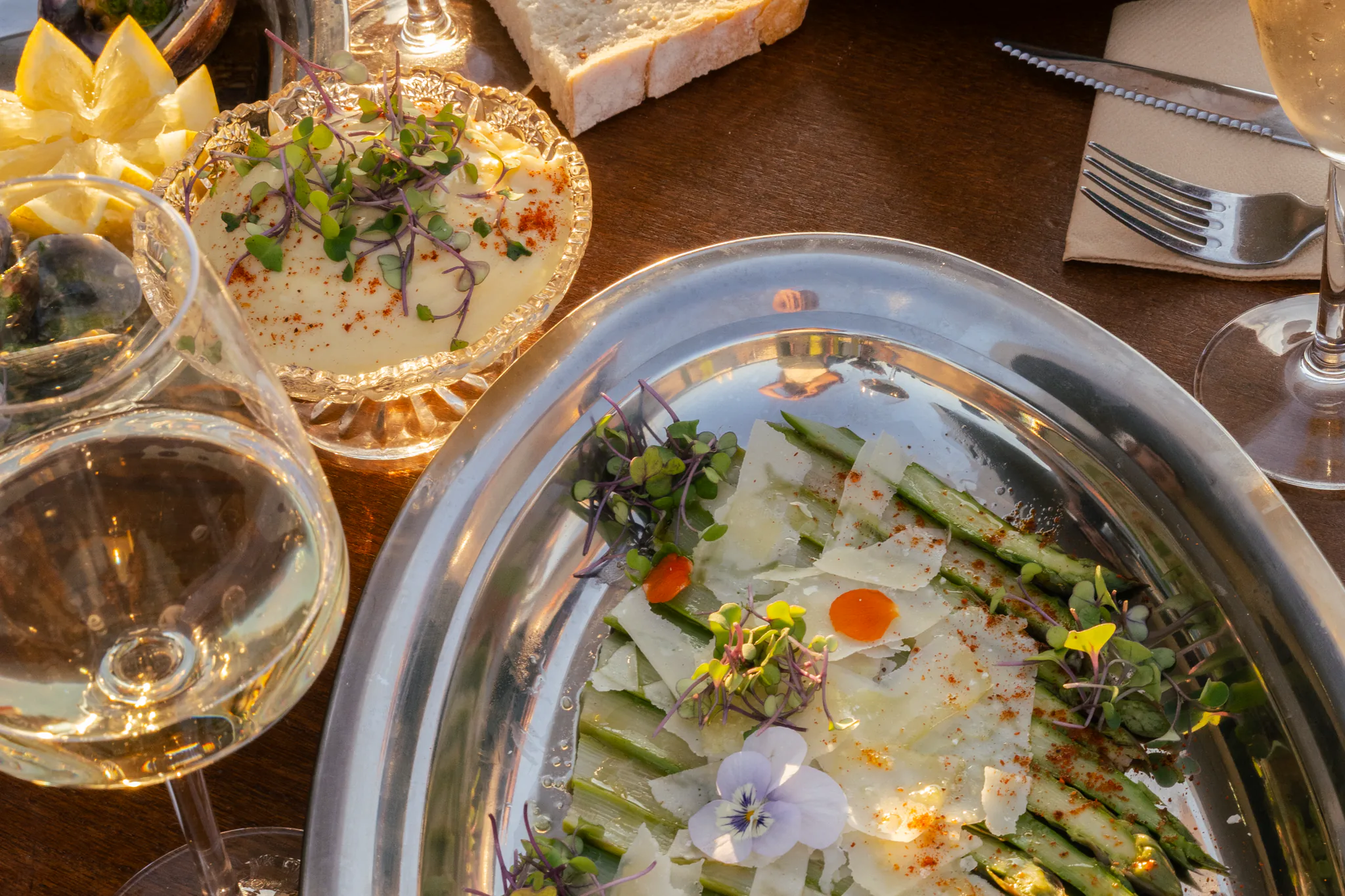 Grand plat d'asperges vertes au parmesan, ceviche et verre de vin blanc sur une table en terrasse