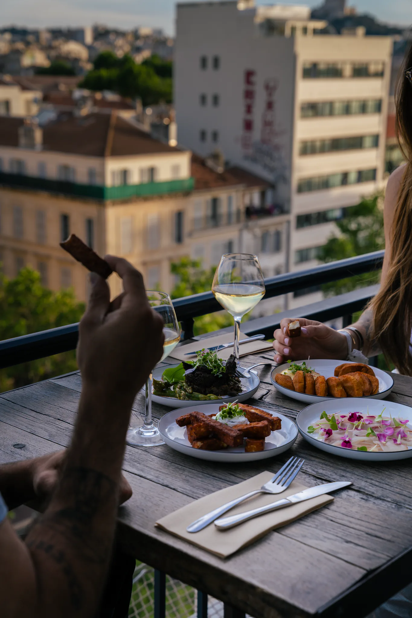 Couple à table en terrasse, assiettes et verre de vin face aux toits au couchant