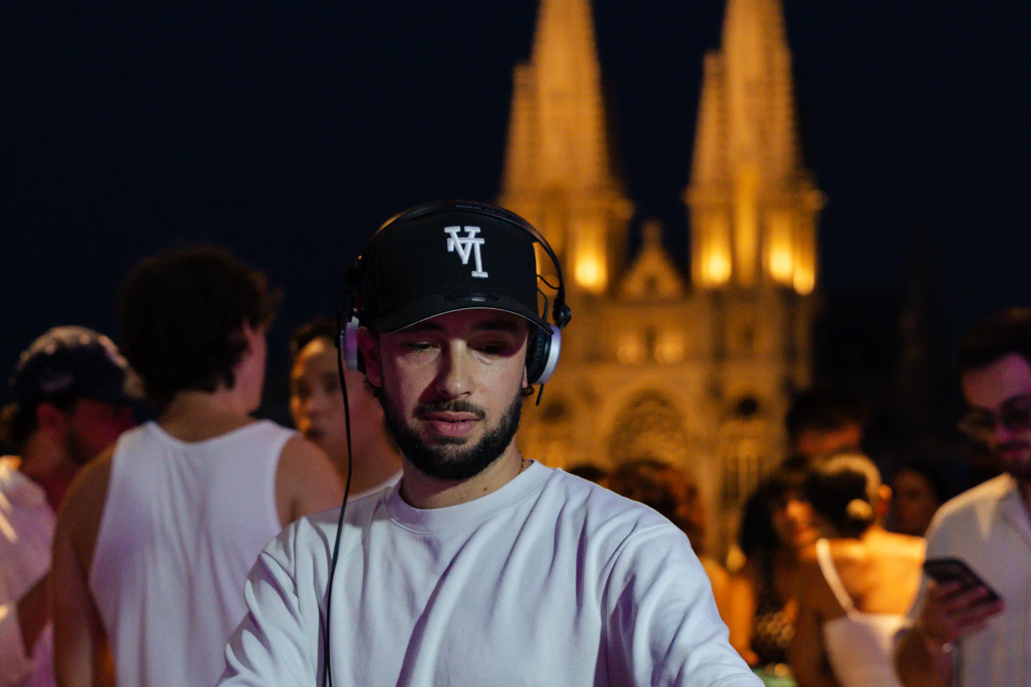 DJ aux platines en terrasse le soir, foule et flèches illuminées de l'église des Réformés en arrière-plan