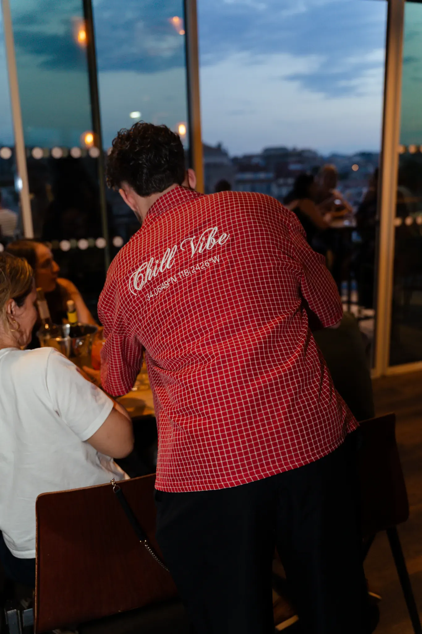 Convives attablés en soirée, la ville au crépuscule derrière les baies