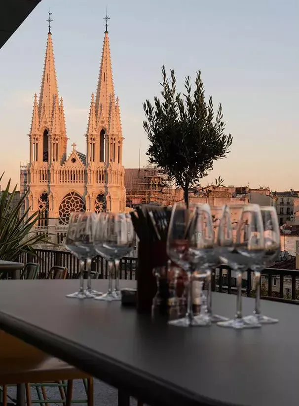 Terrasse de restaurant au coucher du soleil avec verres à vin face aux flèches illuminées d'une église gothique
