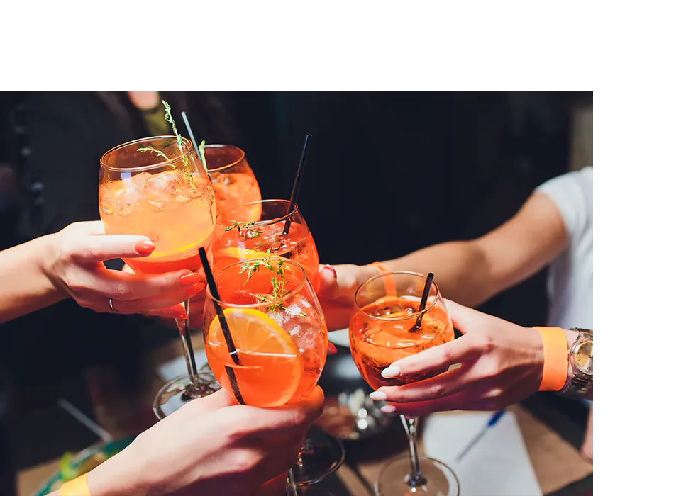 Plusieurs mains brandissent des verres de cocktail orange et trinquent lors d'une soirée festive