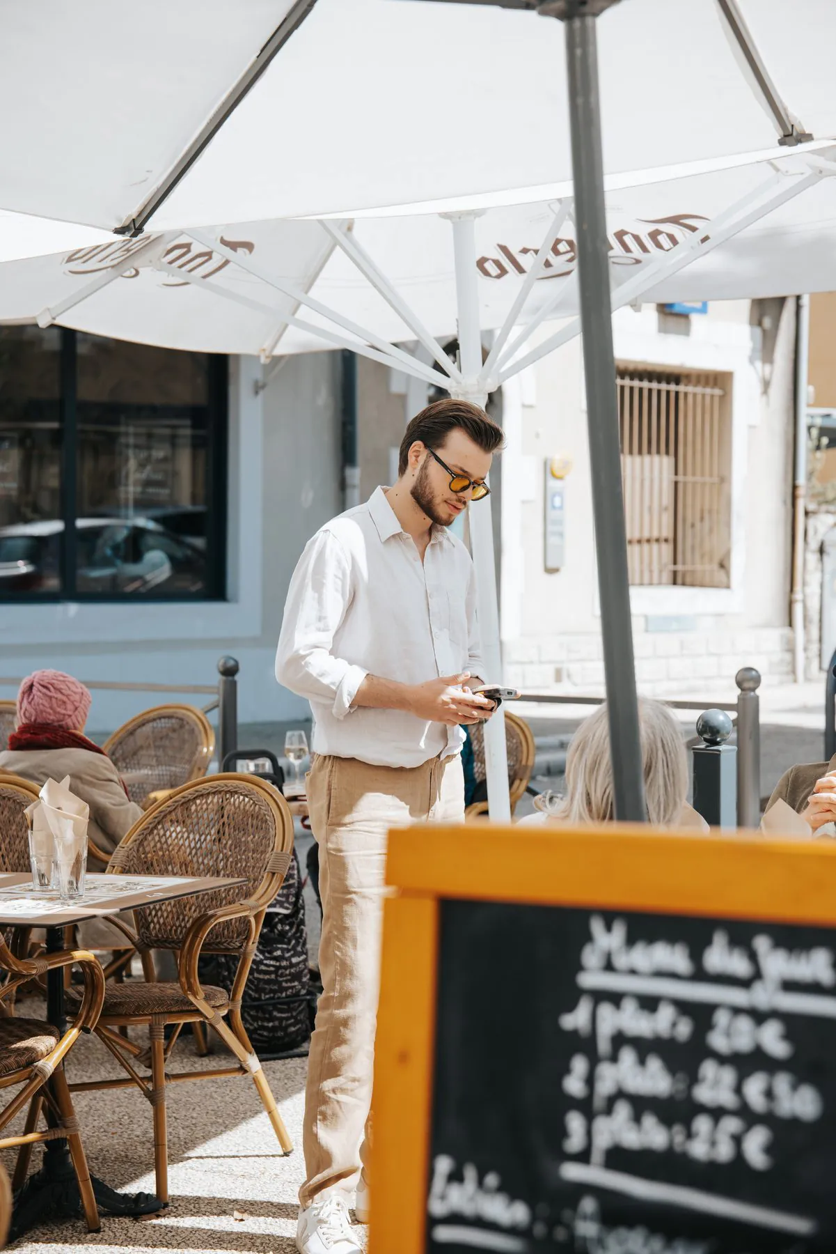 Léo Ricard entre les tables de la terrasse, sous les parasols