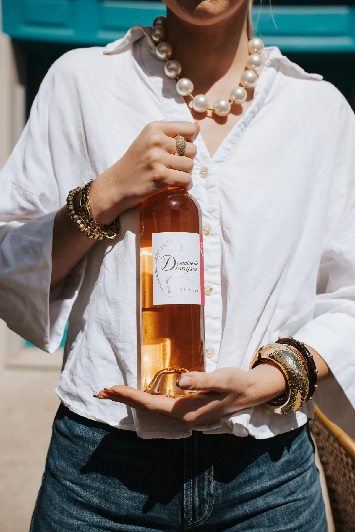 Une bouteille de rosé tenue à deux mains devant la façade turquoise