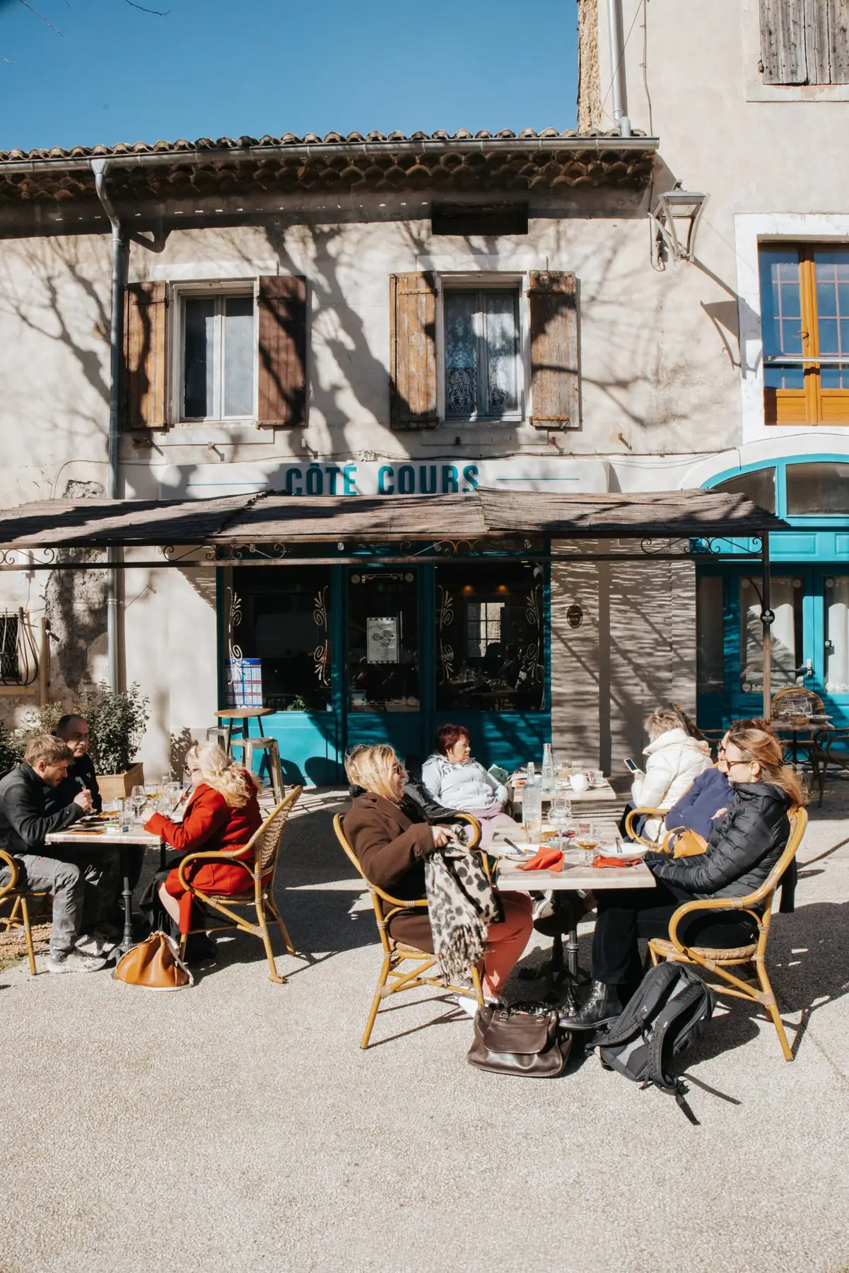 La façade turquoise de Côté Cours et sa terrasse pleine, au soleil