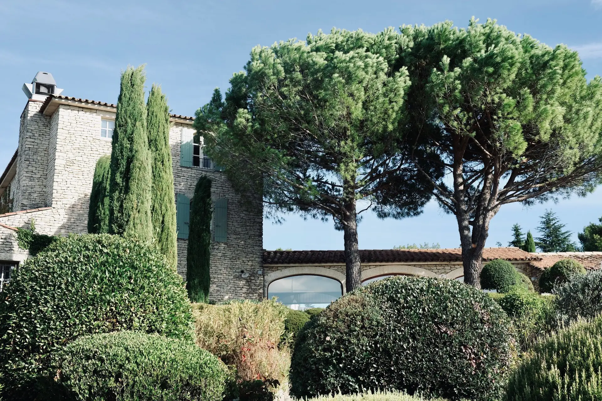 Maison en pierre provençale entourée de cyprès, de pins et de haies taillées en boule