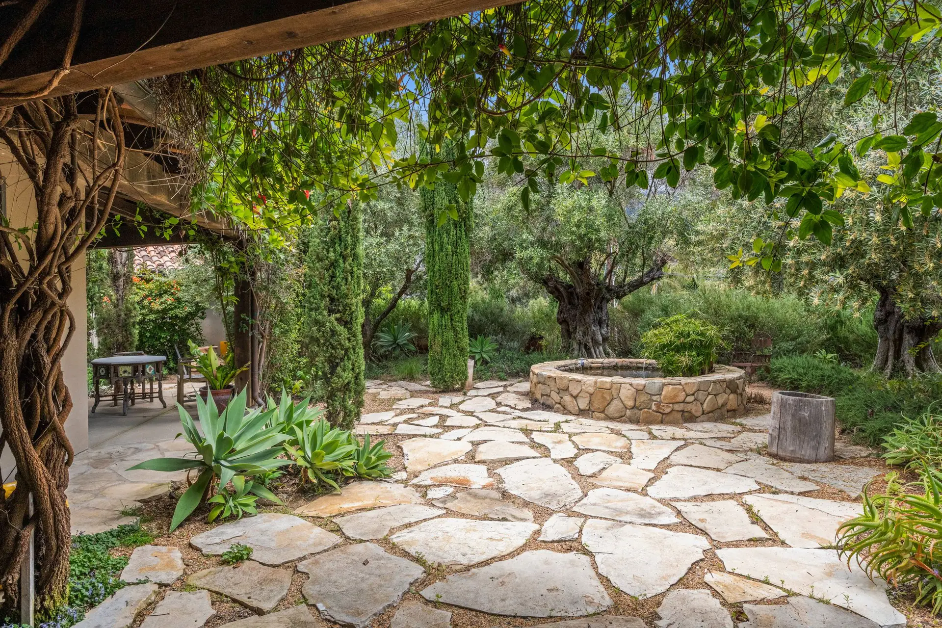 Jardin méditerranéen avec dallage en pierre, oliviers et cyprès sous une pergola
