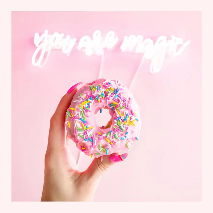 Une main tient un donut à sprinkles devant un néon