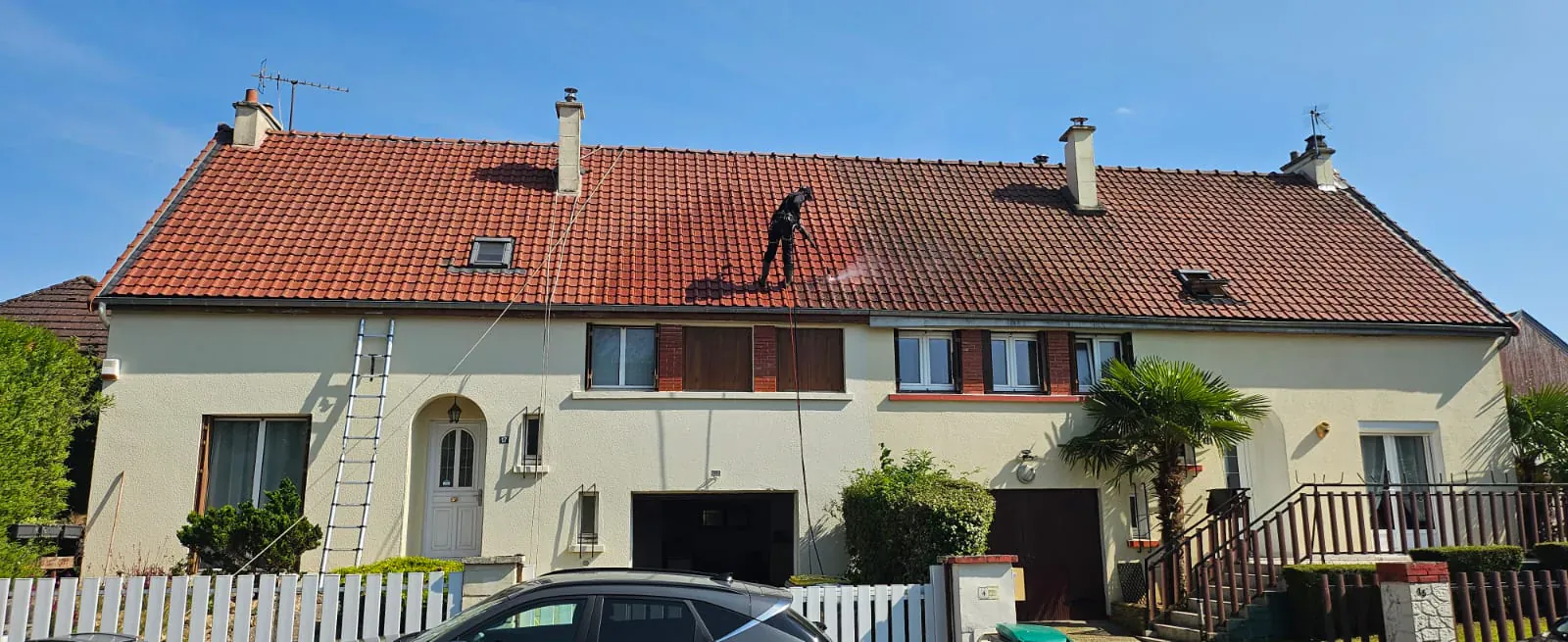 Technicien nettoyant et démoussant au jet la toiture en tuiles rouges d’une maison