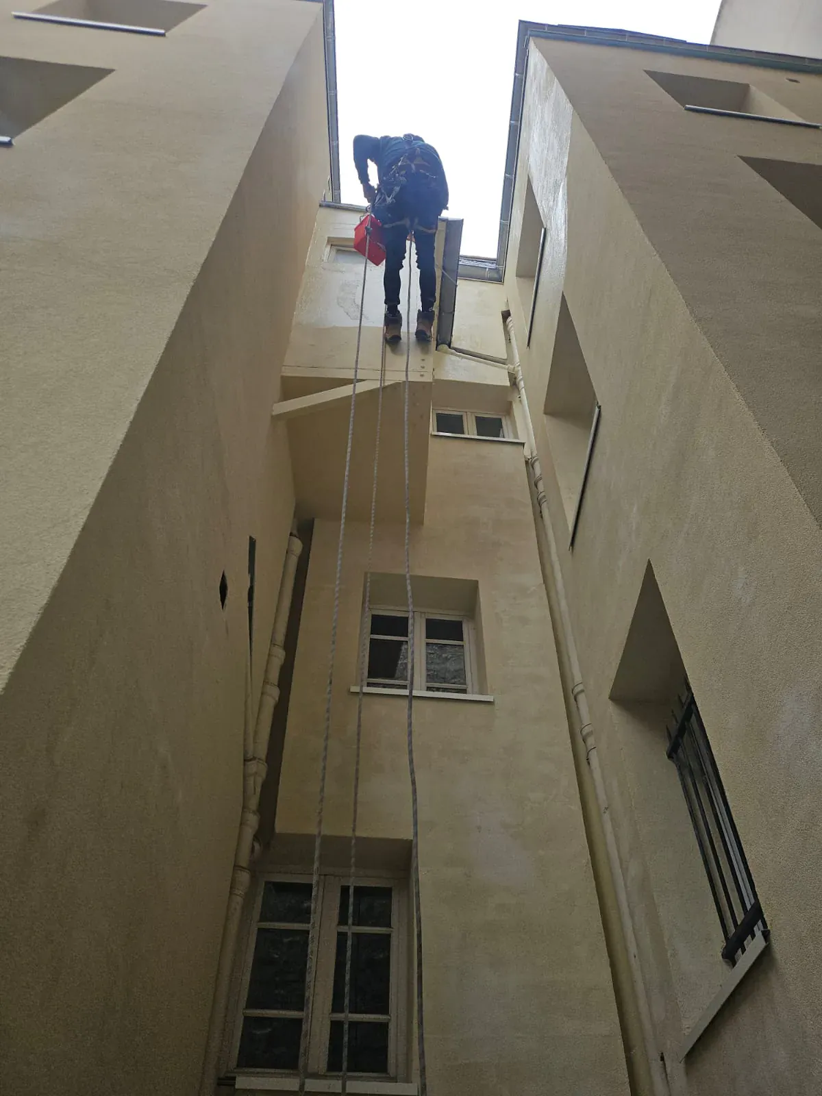 Un technicien cordiste s'apprête à descendre en rappel depuis le sommet d'un immeuble pour intervenir en façade.