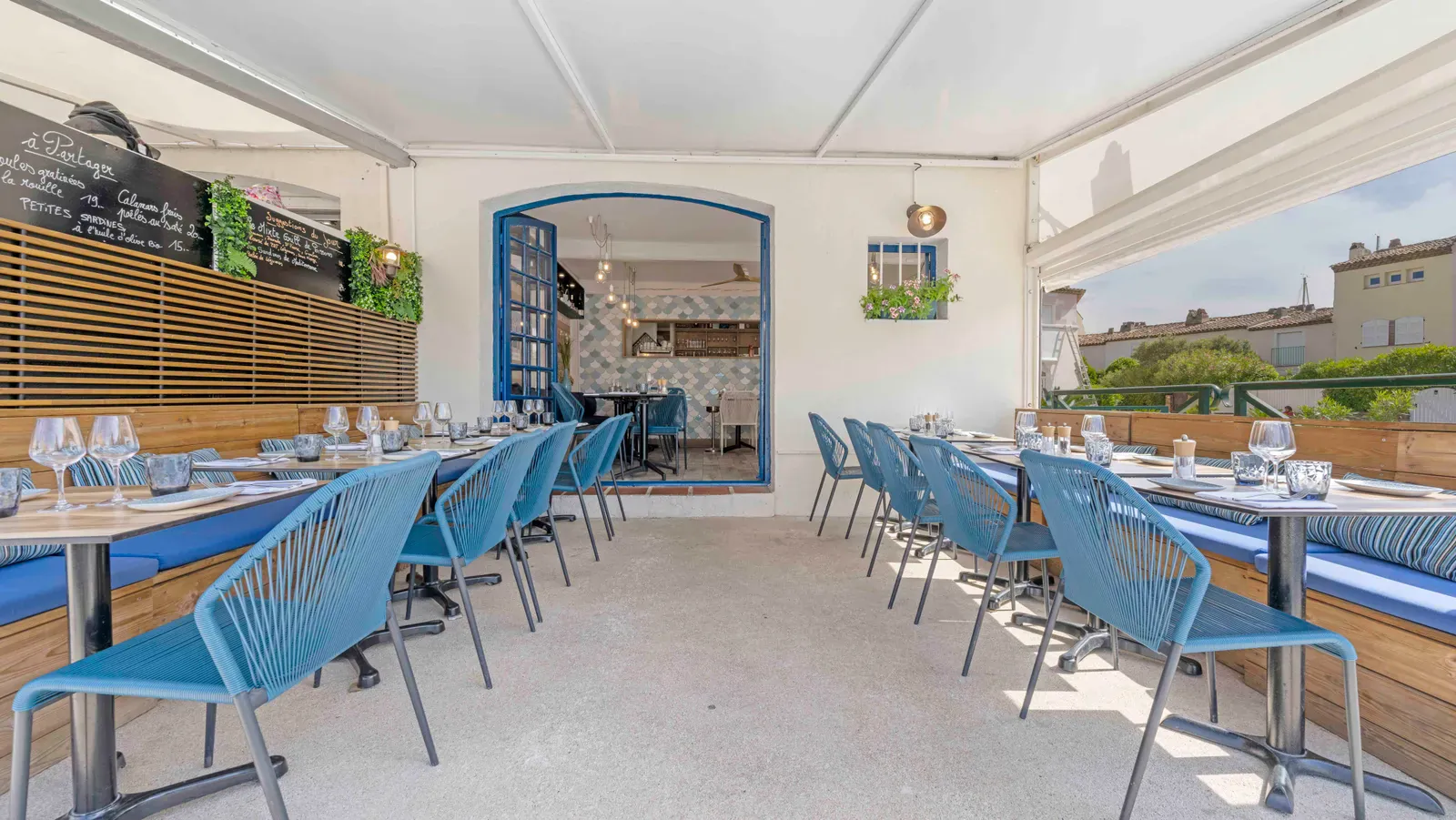 Terrasse couverte du restaurant La Marée à Port Grimaud, chaises bleues, tables dressées et ardoise des suggestions du jour