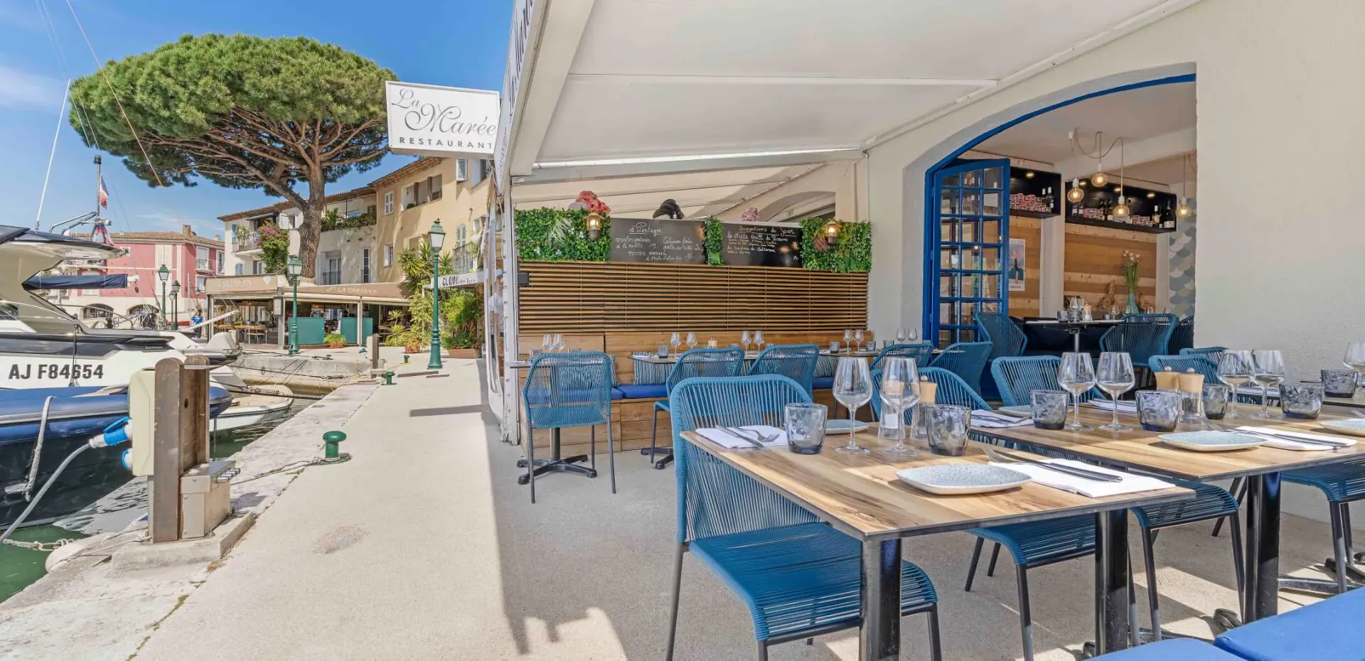 Terrasse ensoleillée du restaurant La Marée face au port de plaisance de Port Grimaud, tables dressées et chaises bleues