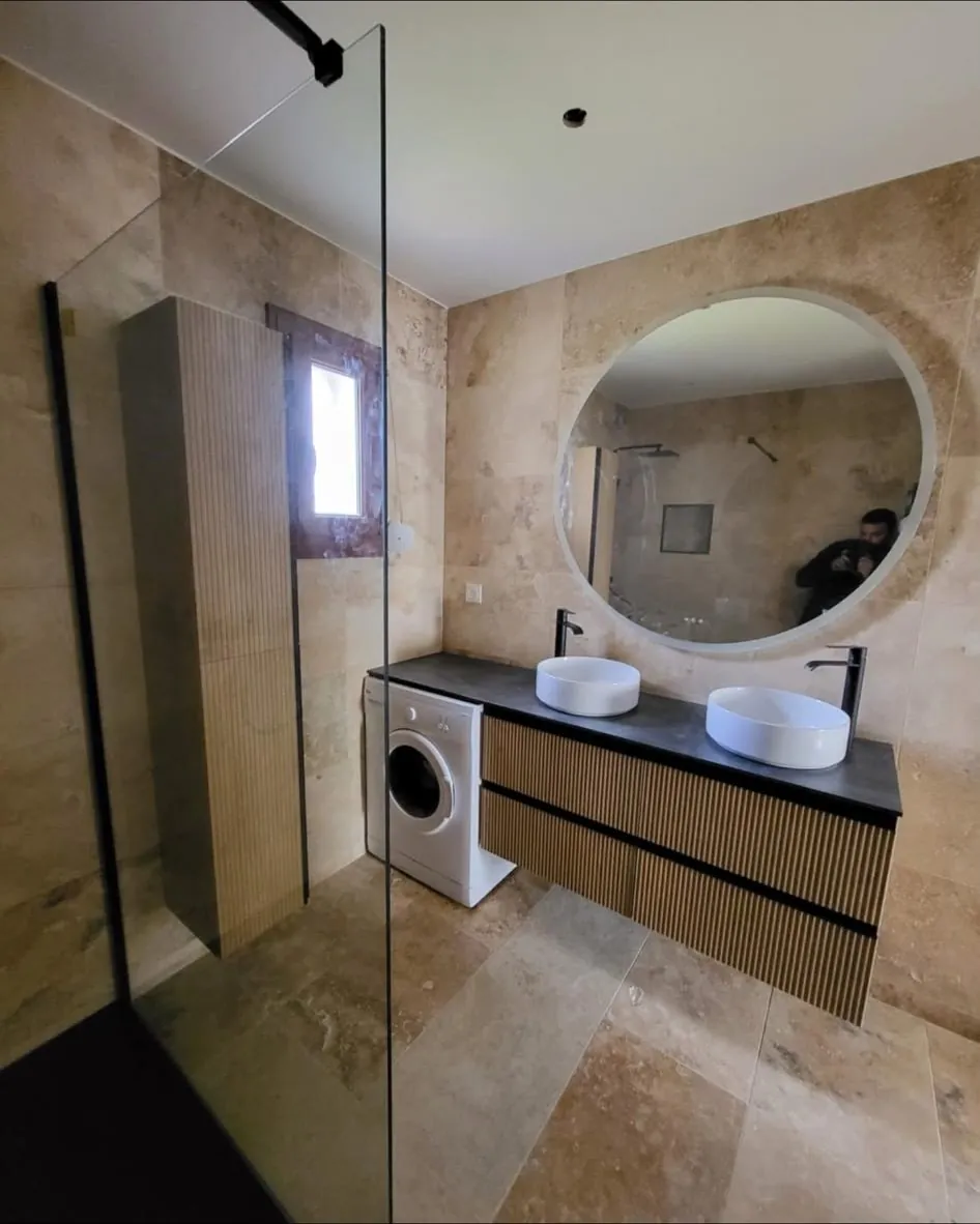 Salle de bain rénovée : double vasque, miroir rond, carrelage pierre