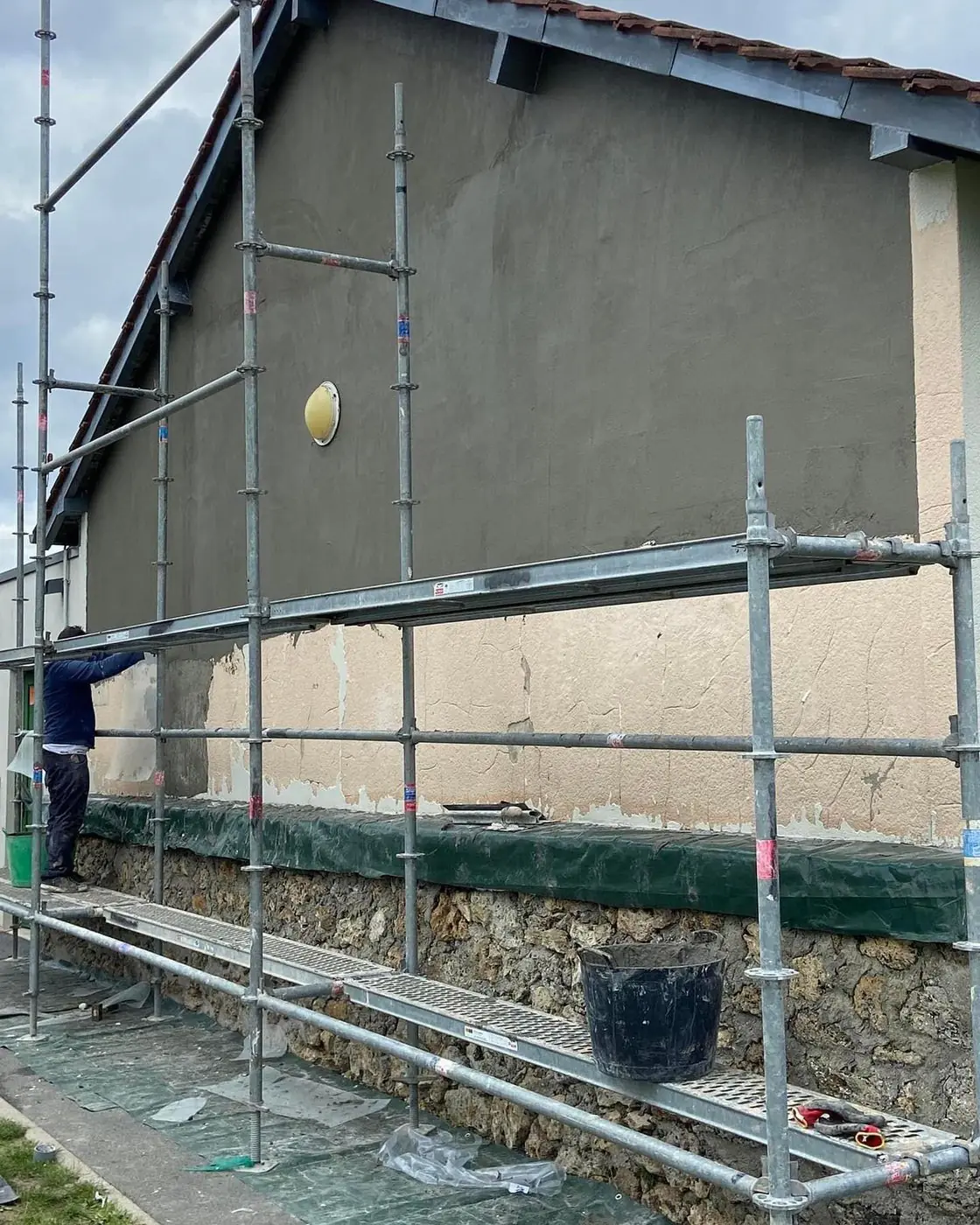 Façade en cours d'enduit sur échafaudage, un ouvrier au travail