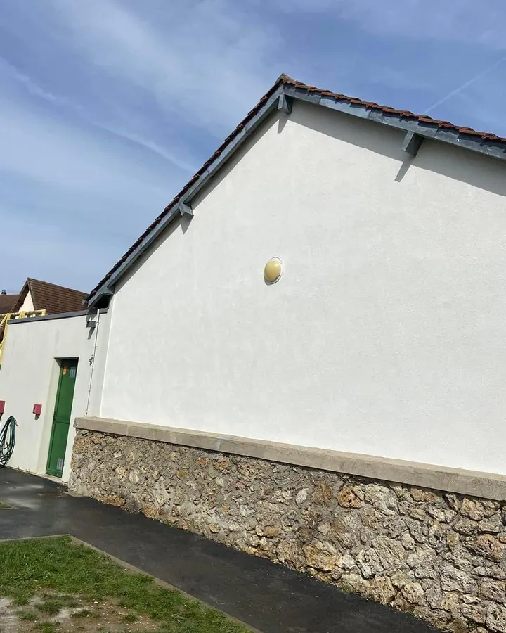 Pignon de bâtiment fraîchement enduit en blanc lisse, au-dessus d'un soubassement en pierre