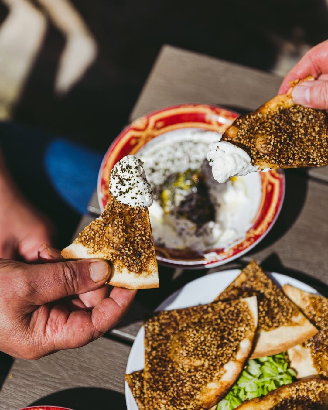 Deux mains partagent une manakish za'atar trempée dans le labneh