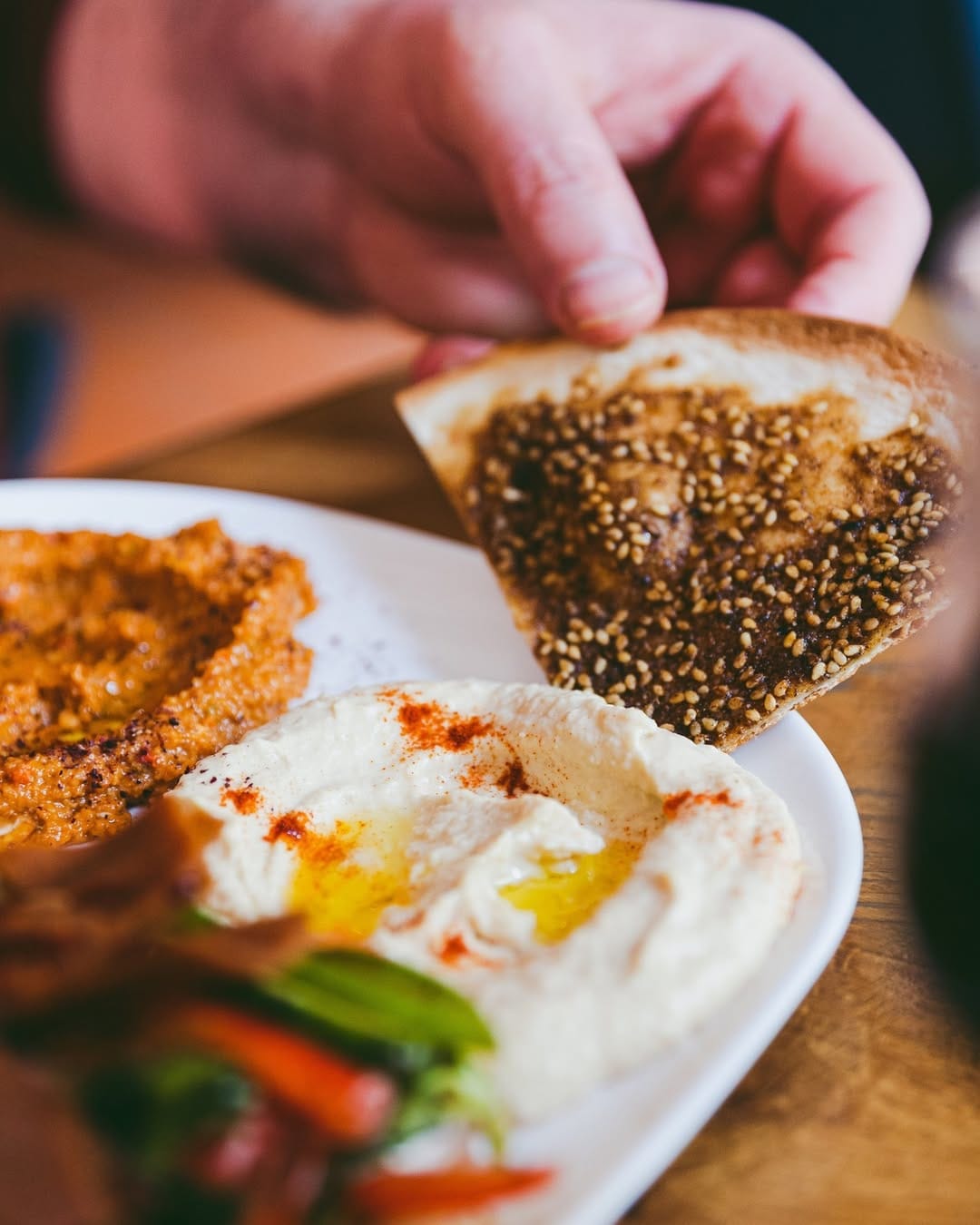 Une main trempe une manakish za'atar dans le houmous