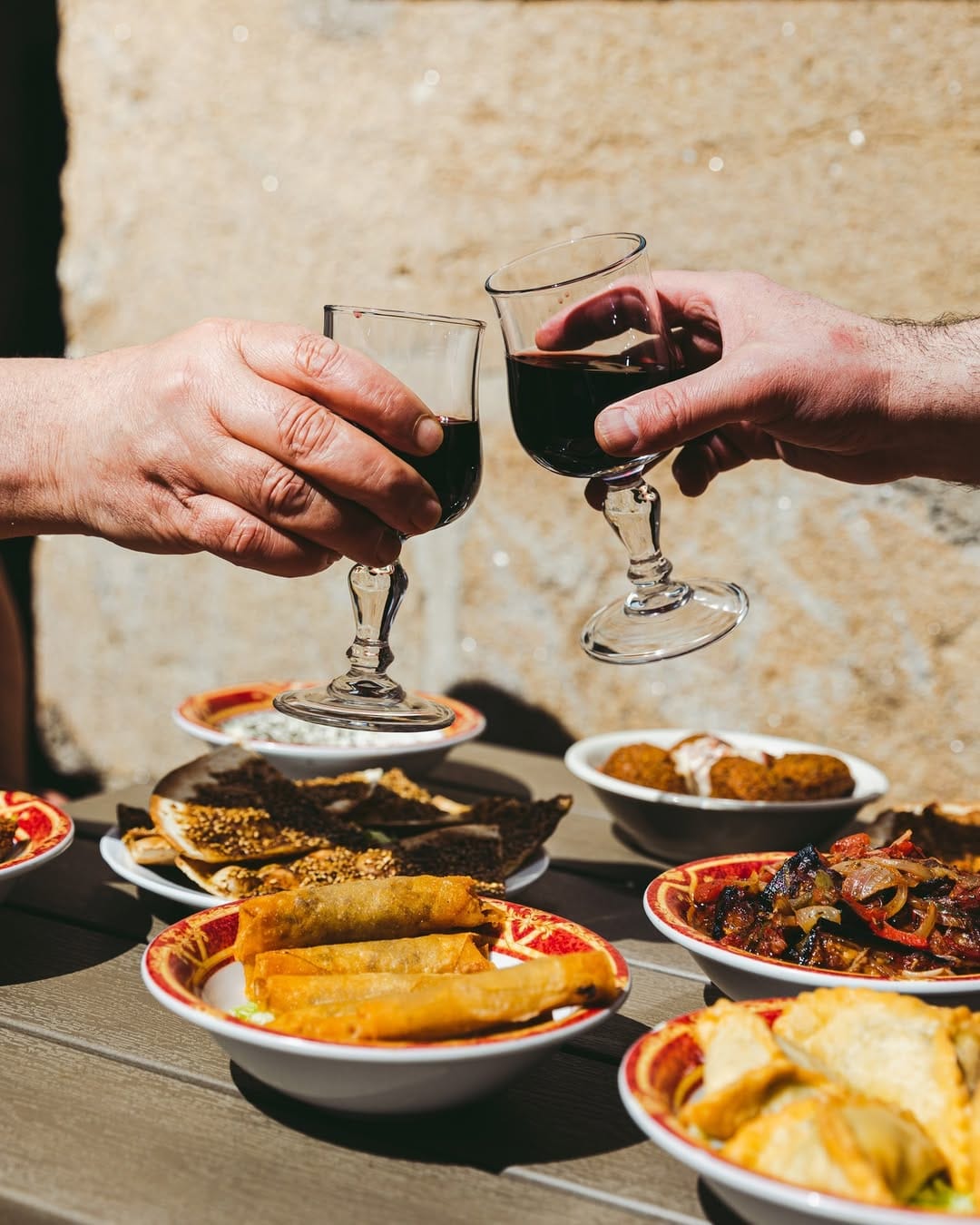 Deux mains trinquent au vin au-dessus d'une table couverte de mezzés