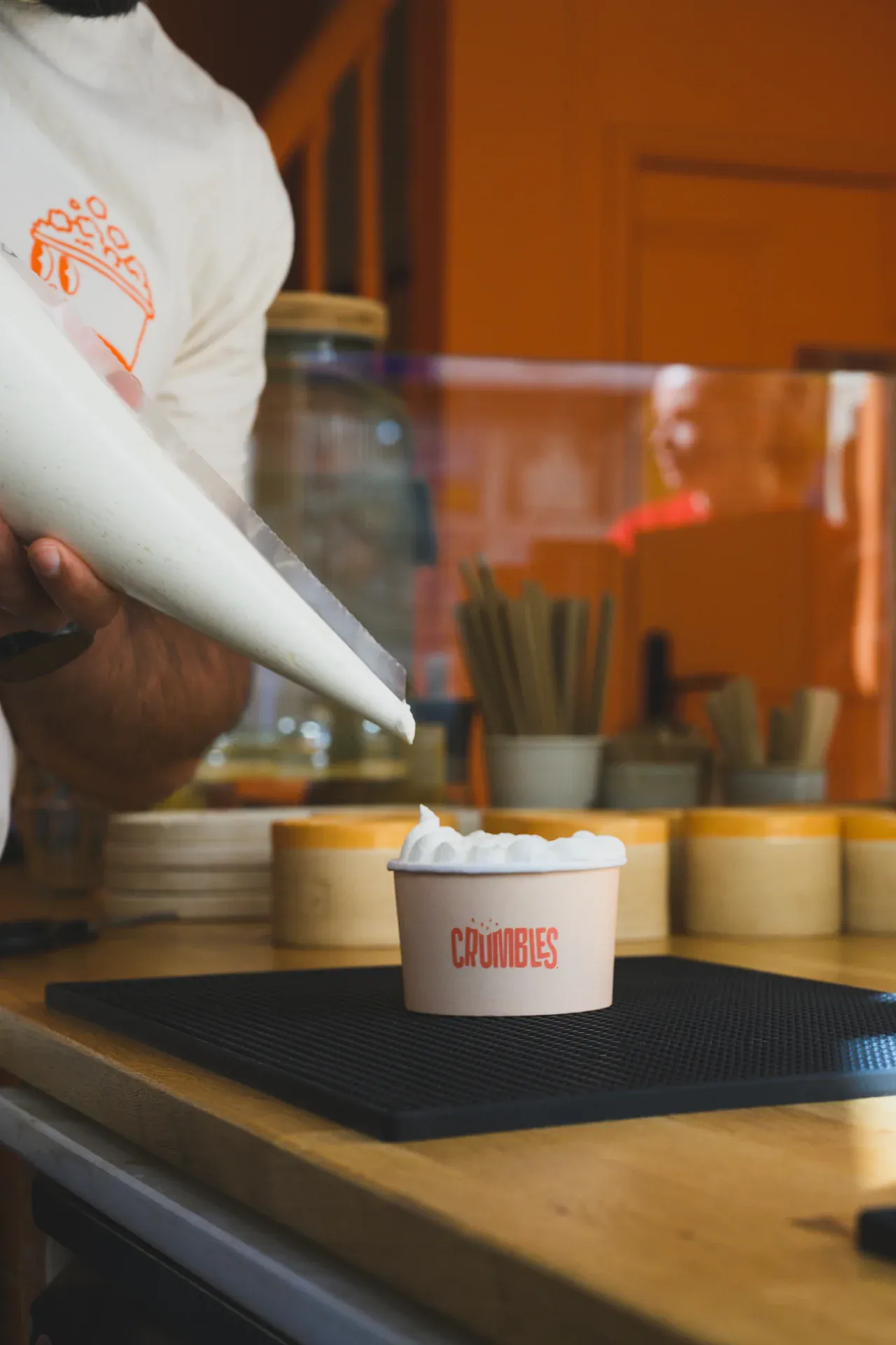Un membre de l'équipe Crumbles garnit un dessert à la poche à douille au comptoir