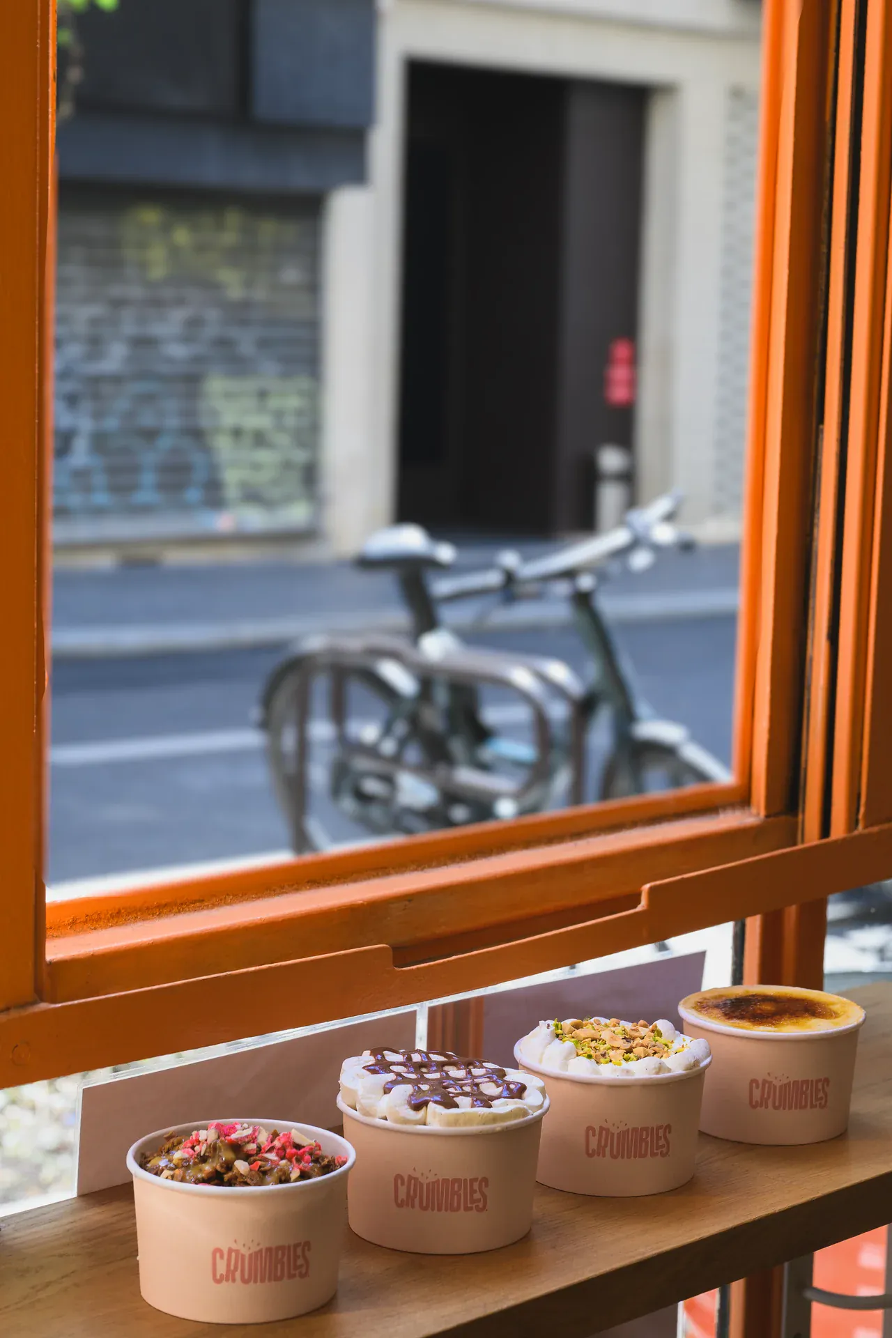 La devanture orange du café Crumbles dans une rue du 9e arrondissement de Paris, un vélo garé devant