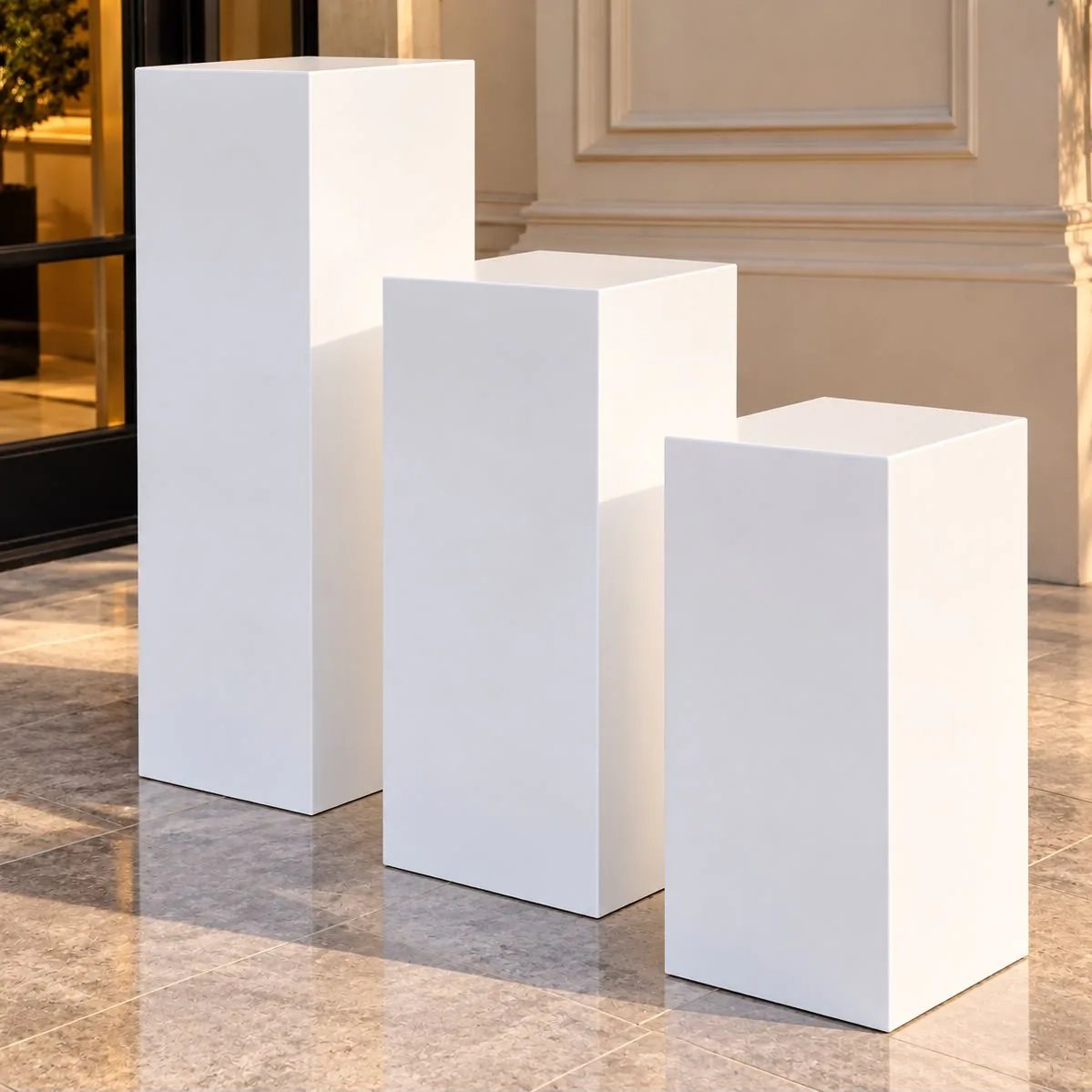 Trois colonnes rectangulaires blanches de hauteurs différentes, posées sur un sol en pierre claire.