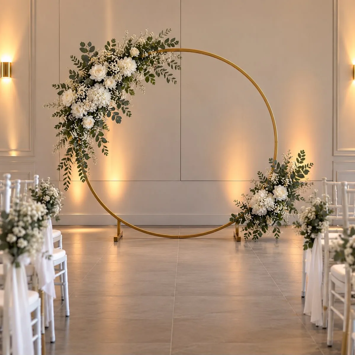 Arche ronde dorée habillée de fleurs blanches et de feuillage, au bout d'une allée de cérémonie bordée de chaises blanches.