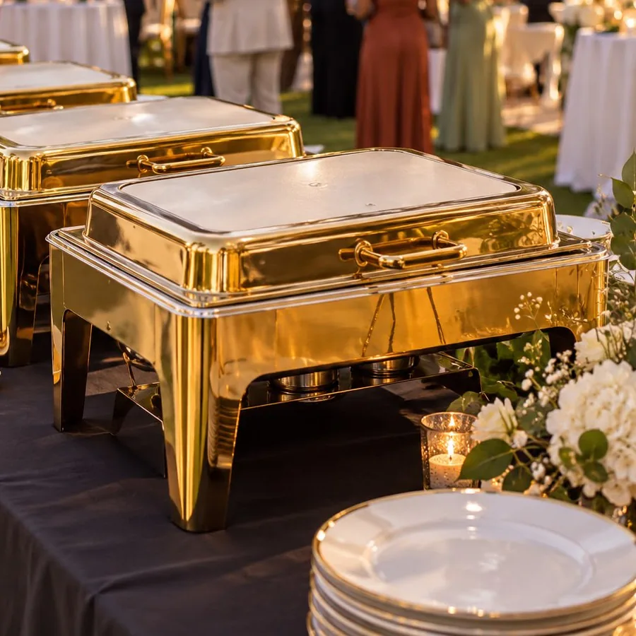 Chauffe-plats rectangulaires dorés alignés sur un buffet de réception en extérieur.