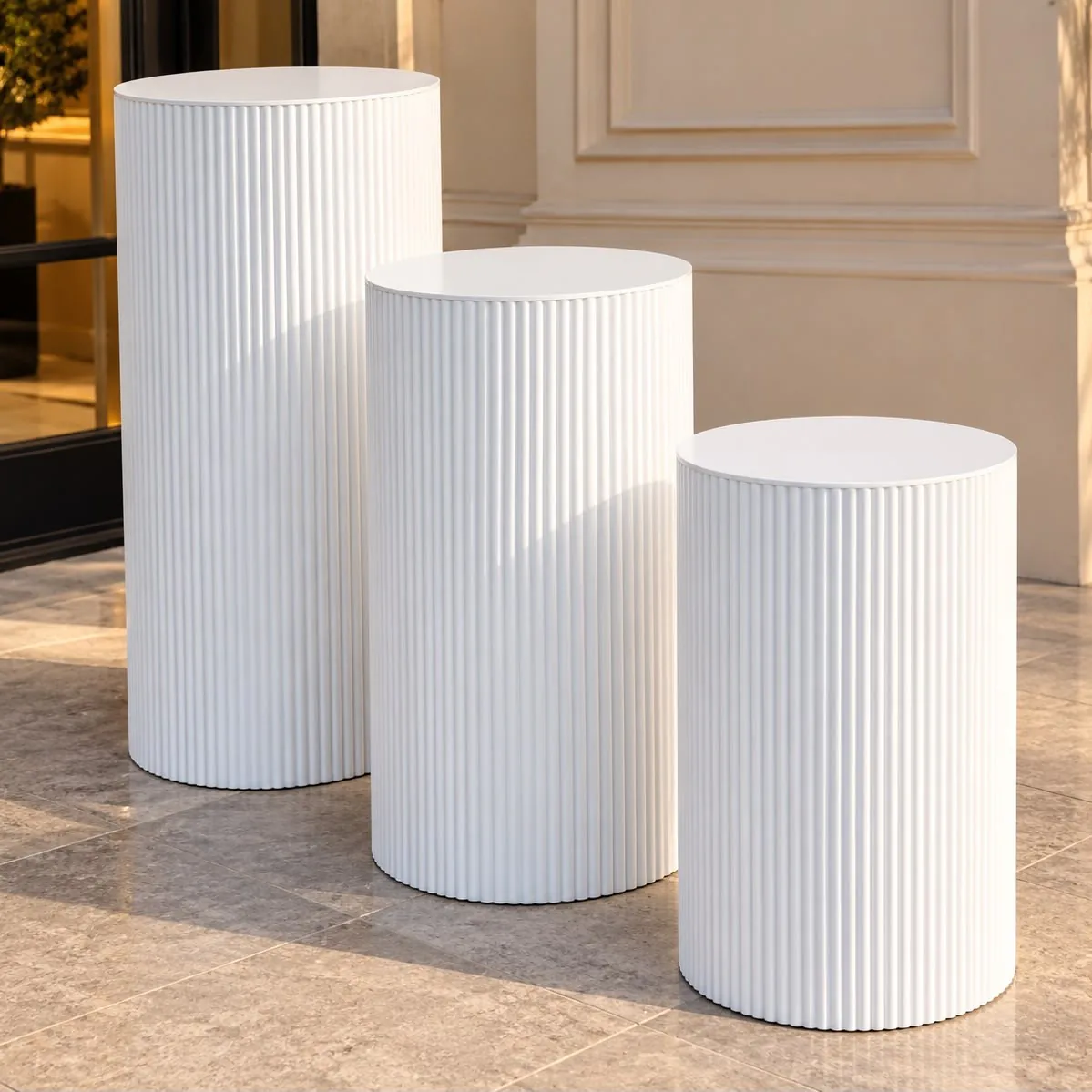Trois colonnes cylindriques blanches cannelées de hauteurs différentes, posées sur un sol en pierre claire.