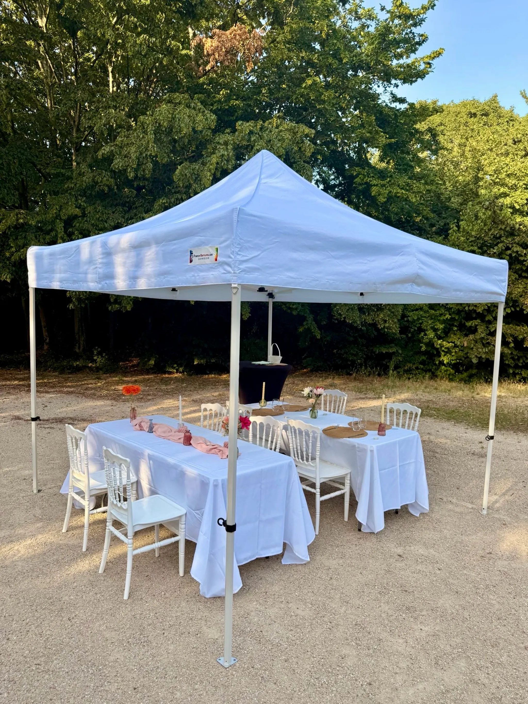 Réception en extérieur : tonnelle blanche 3 × 3, tables rectangulaires nappées de blanc, chaises Napoléon et chemin de table rose poudré.