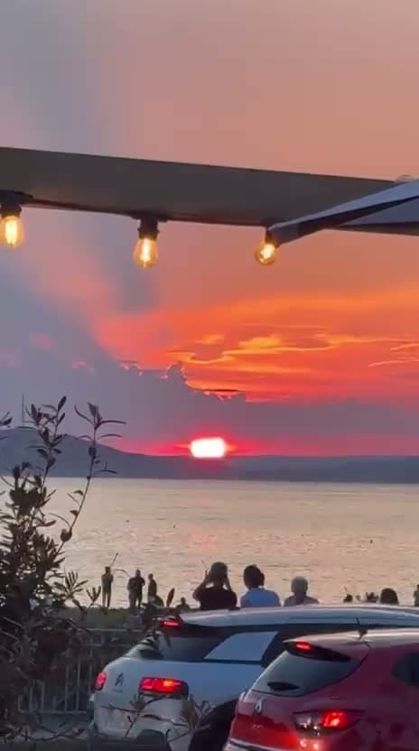 Coucher de soleil sur la mer observé depuis une terrasse ornée d'une guirlande lumineuse à l'Estéou.