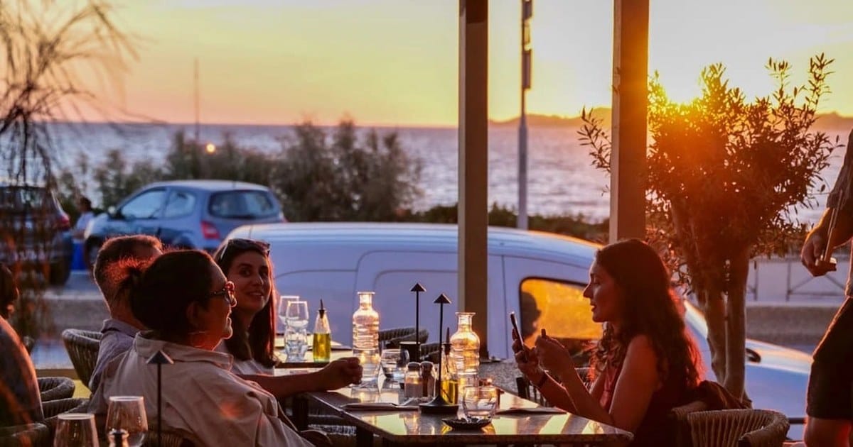 Des clients dînent en terrasse face à la mer au coucher du soleil à l'Estéou, restaurant bord de mer à Marseille.
