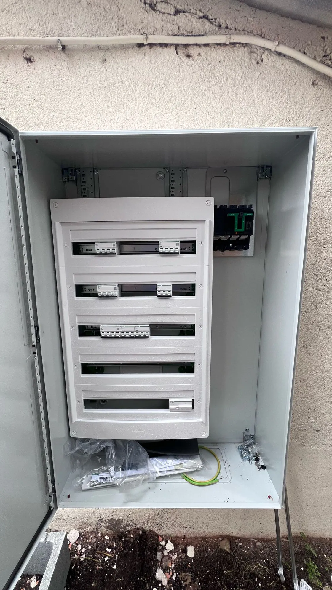 Une armoire métallique grise ouverte, coffret Schneider encore peu équipé.