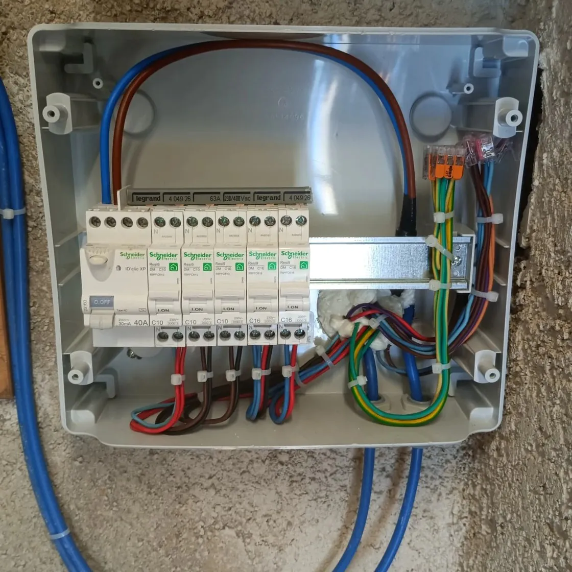 Un coffret de tableau gris ouvert, disjoncteurs neufs.