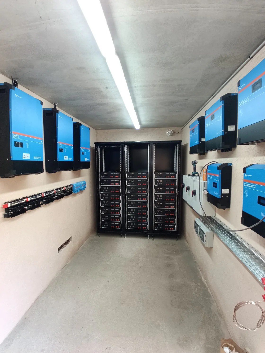 Un local technique étroit, trois baies de batteries au fond, onduleurs bleus aux murs.