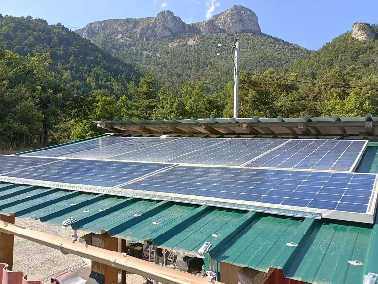 Champ de panneaux solaires sur une toiture en tôle verte, en lisière de forêt