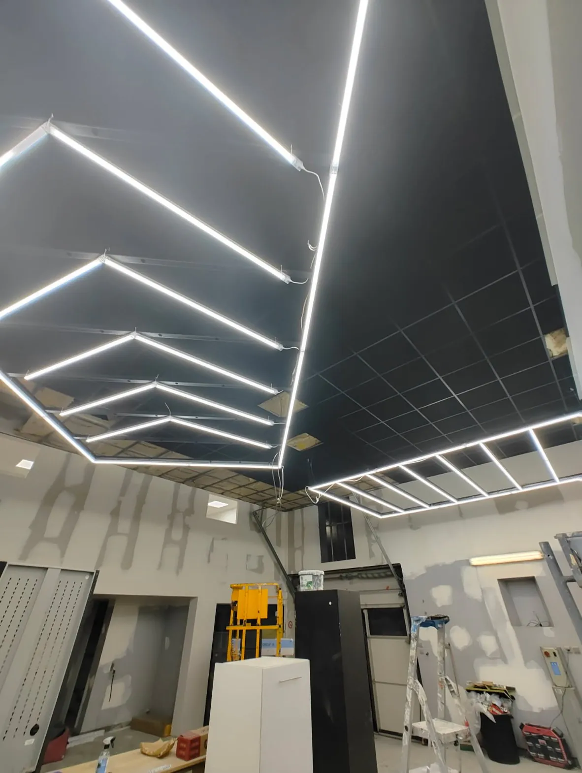 Cadre lumineux à barreaux en chevrons posé dans un faux plafond sombre.