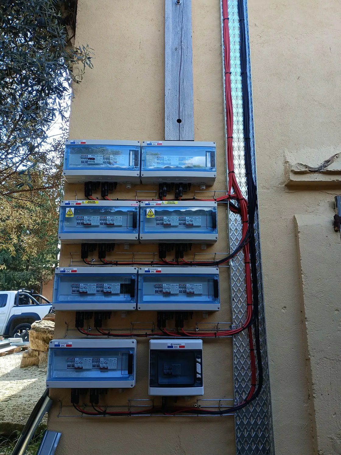 Huit coffrets gris étiquetés DC, raccordés sur une façade enduite ocre.